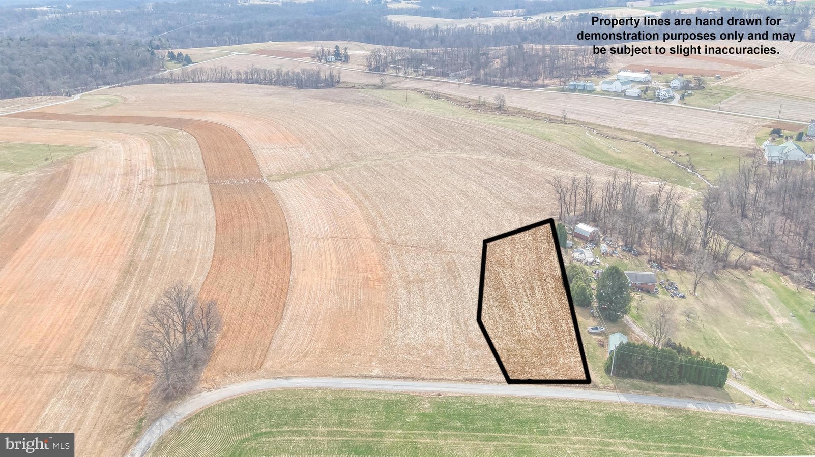 Aerial view of a plowed farmland with a hand-drawn outlined parcel along a road near a cluster of houses, shown for demonstration purposes.