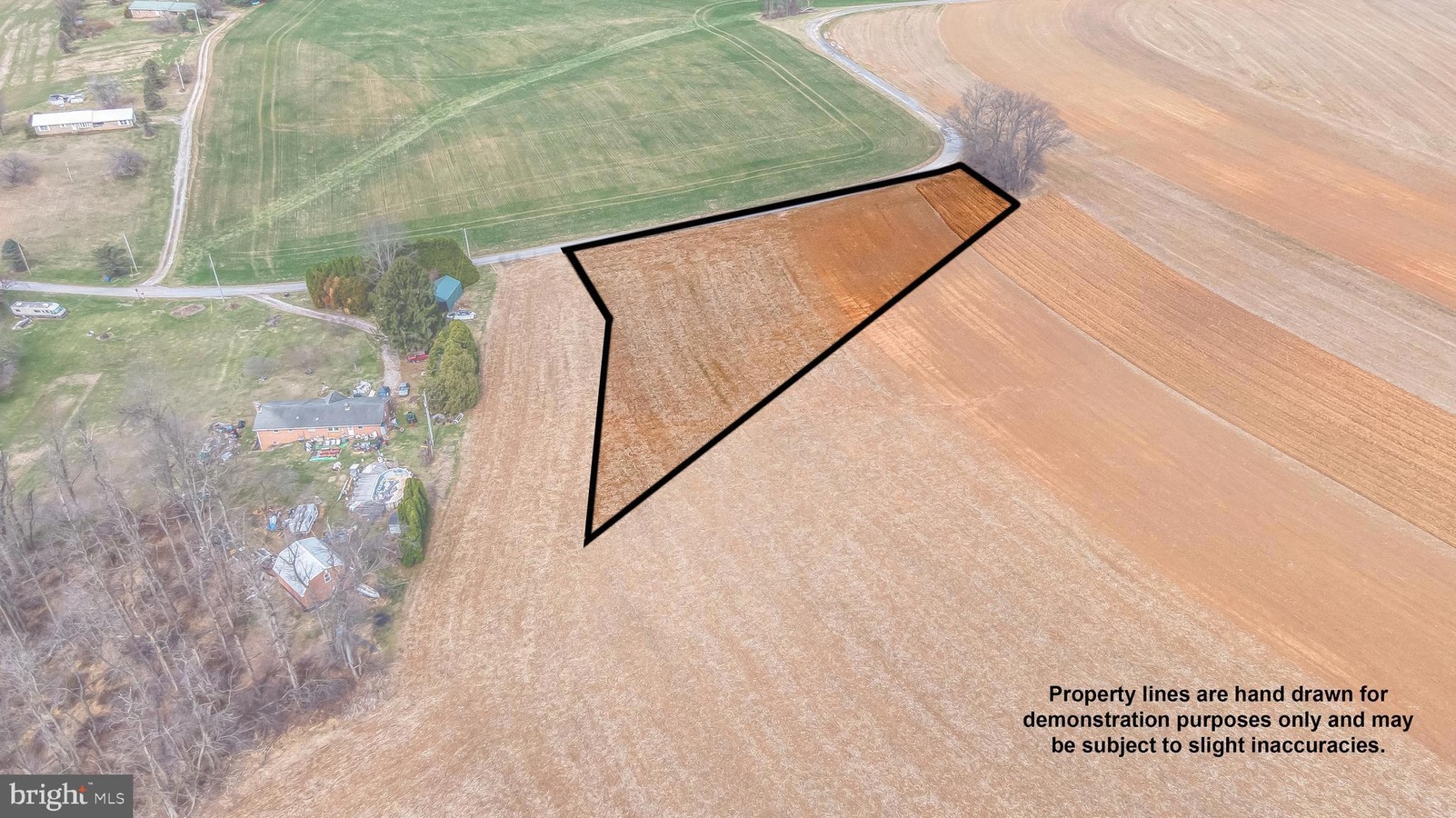 Aerial view showing a brown harvested field with a bold black polygon outlining a lot, set beside green fields and a house lot; caption notes demonstration lines are approximate.