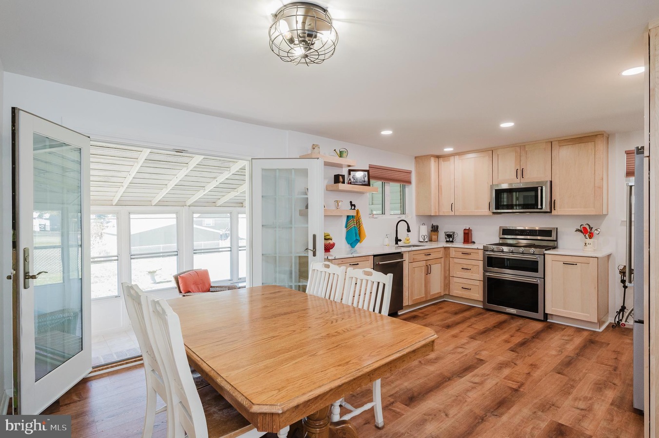 Bright kitchen with light wood cabinets, stainless steel stove/oven, and a wooden dining table with white chairs in an open-plan space