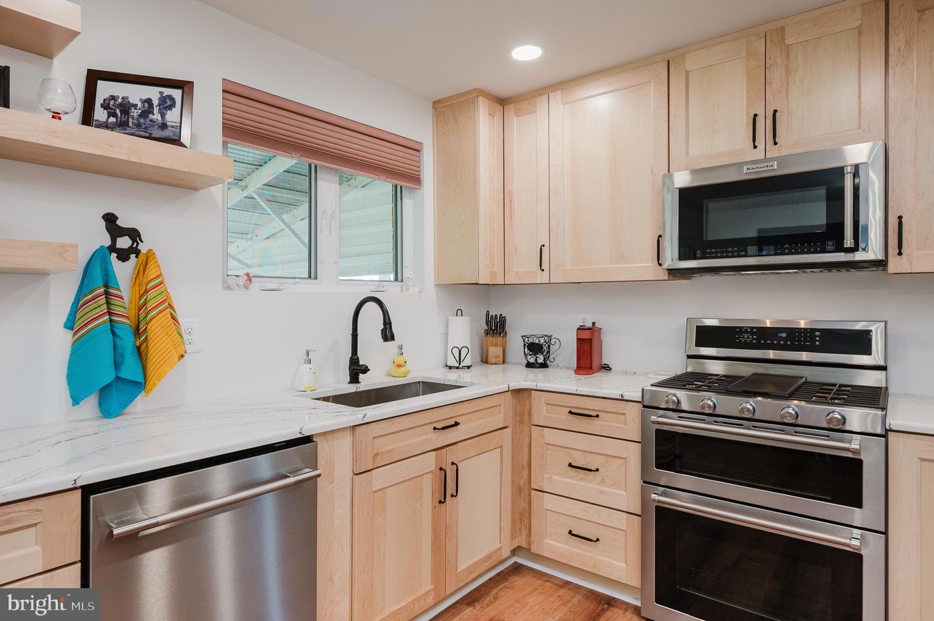 Modern kitchen with light wood cabinets, stainless steel double-oven range and microwave, white marble counters, and a window.