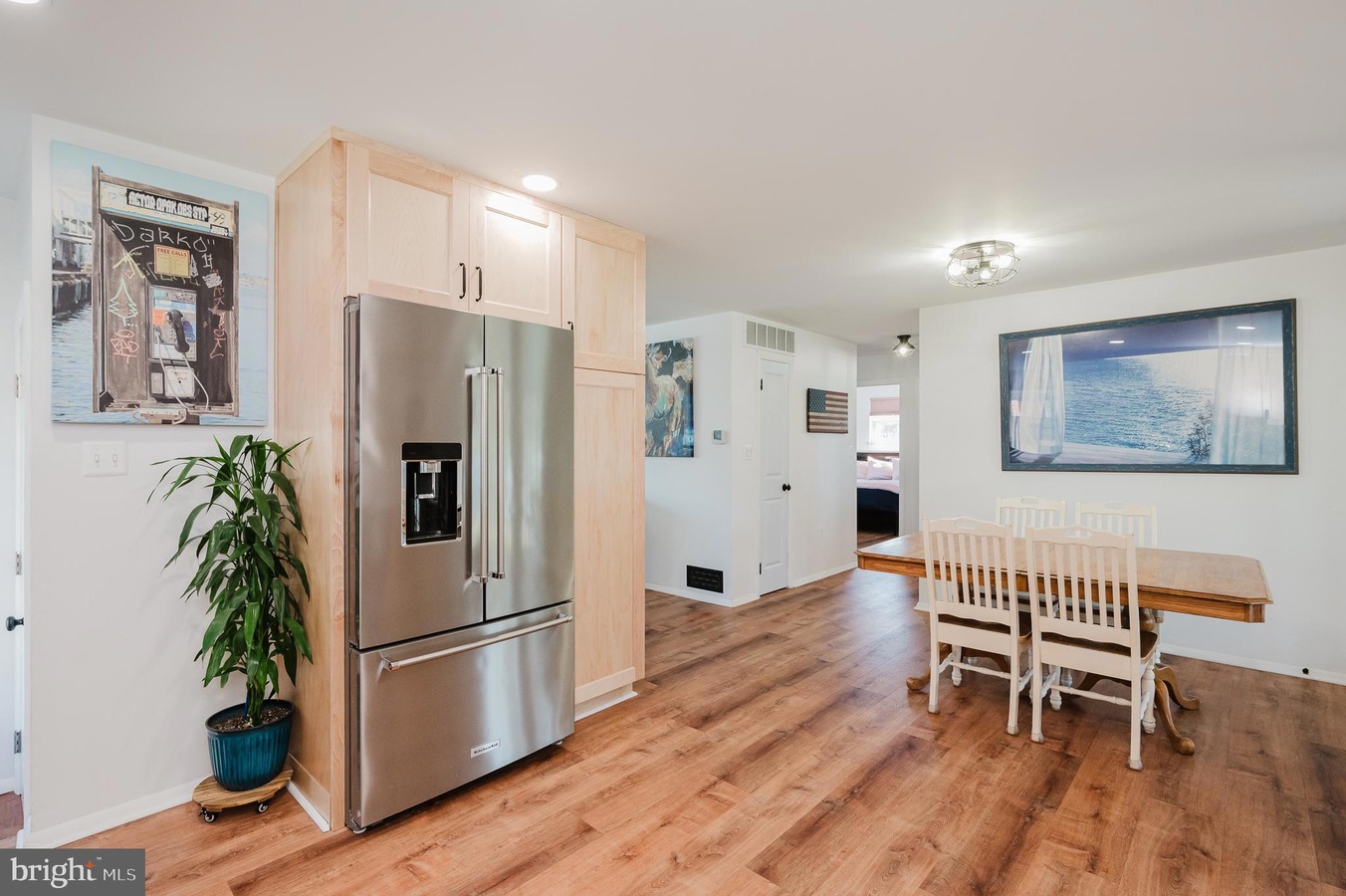 Kitchen with stainless steel French-door refrigerator, light wood cabinets, and a potted plant beside it.