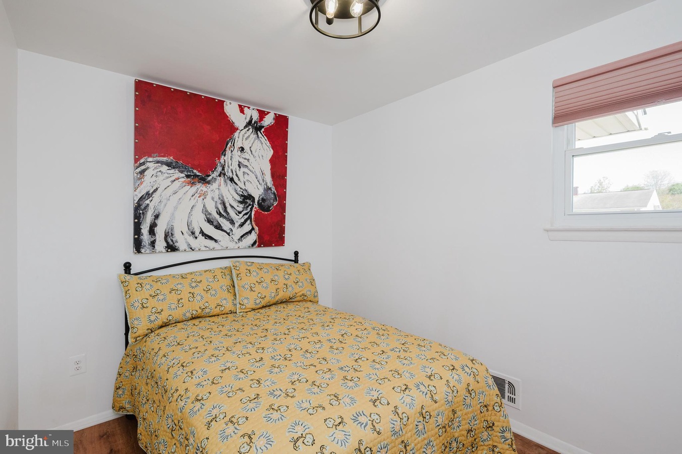 Small bedroom with a black metal bed, yellow floral duvet and pillows, and a red-and-white zebra painting above the headboard.