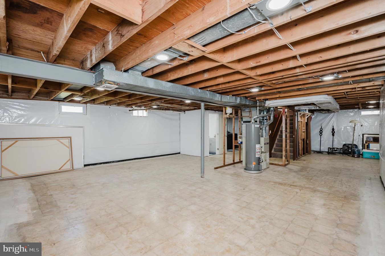 Unfinished basement with exposed wooden joists, a central furnace, and utility area along the back wall.
