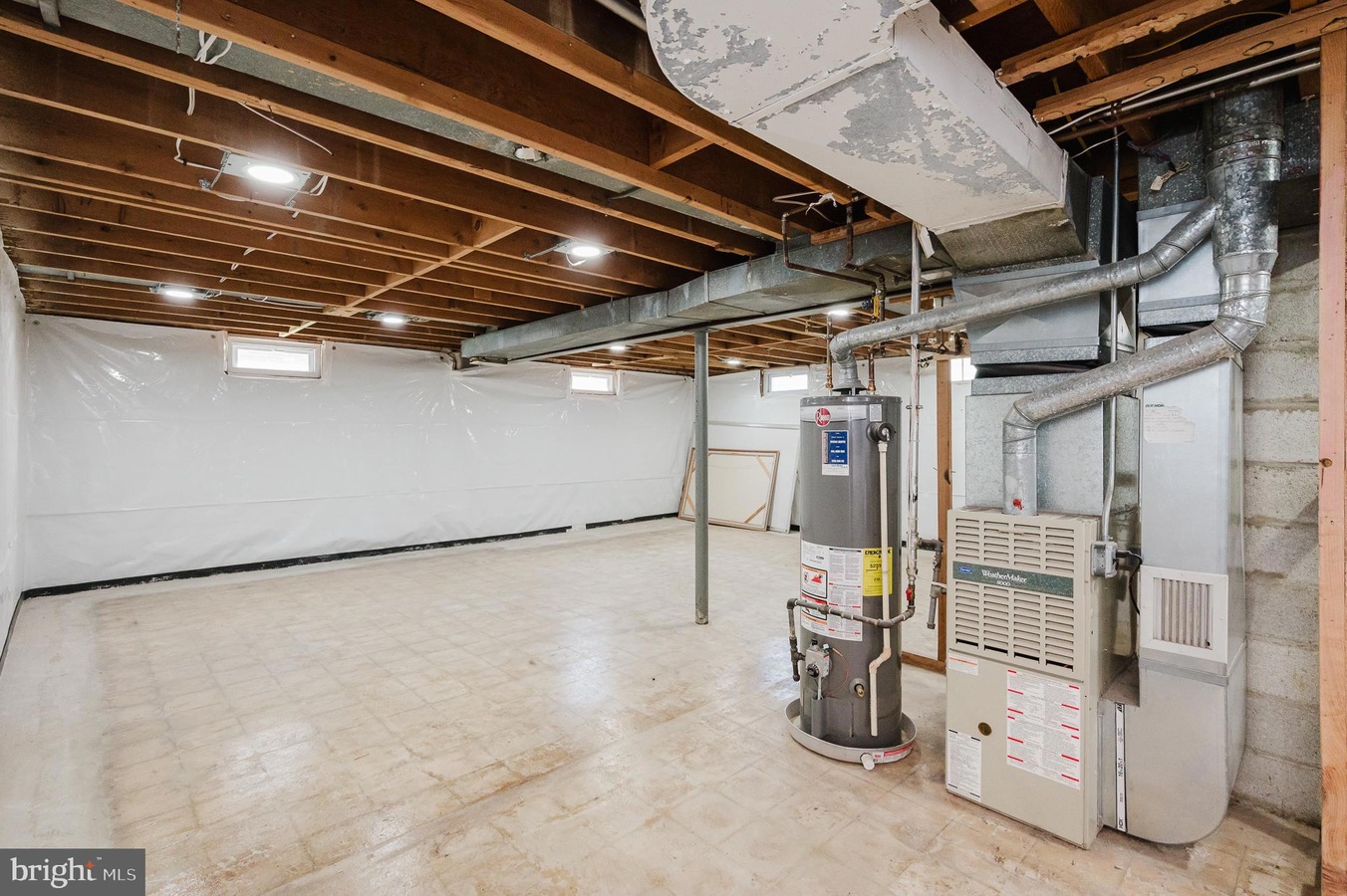 Unfinished basement utility area with exposed ceiling joists, ductwork, and a water heater next to a furnace.