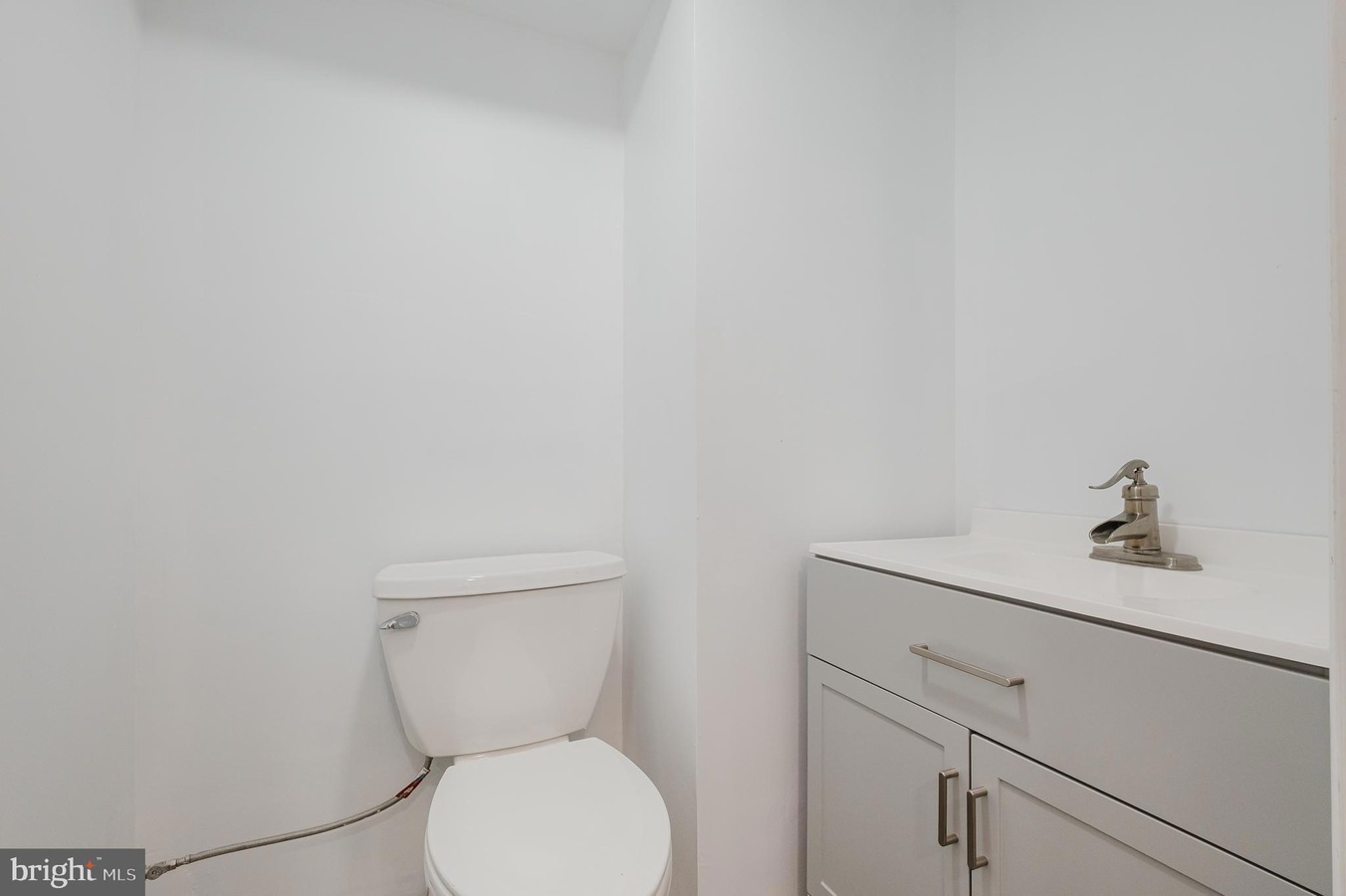 Small white bathroom with a toilet beside a light gray vanity and sink faucet.