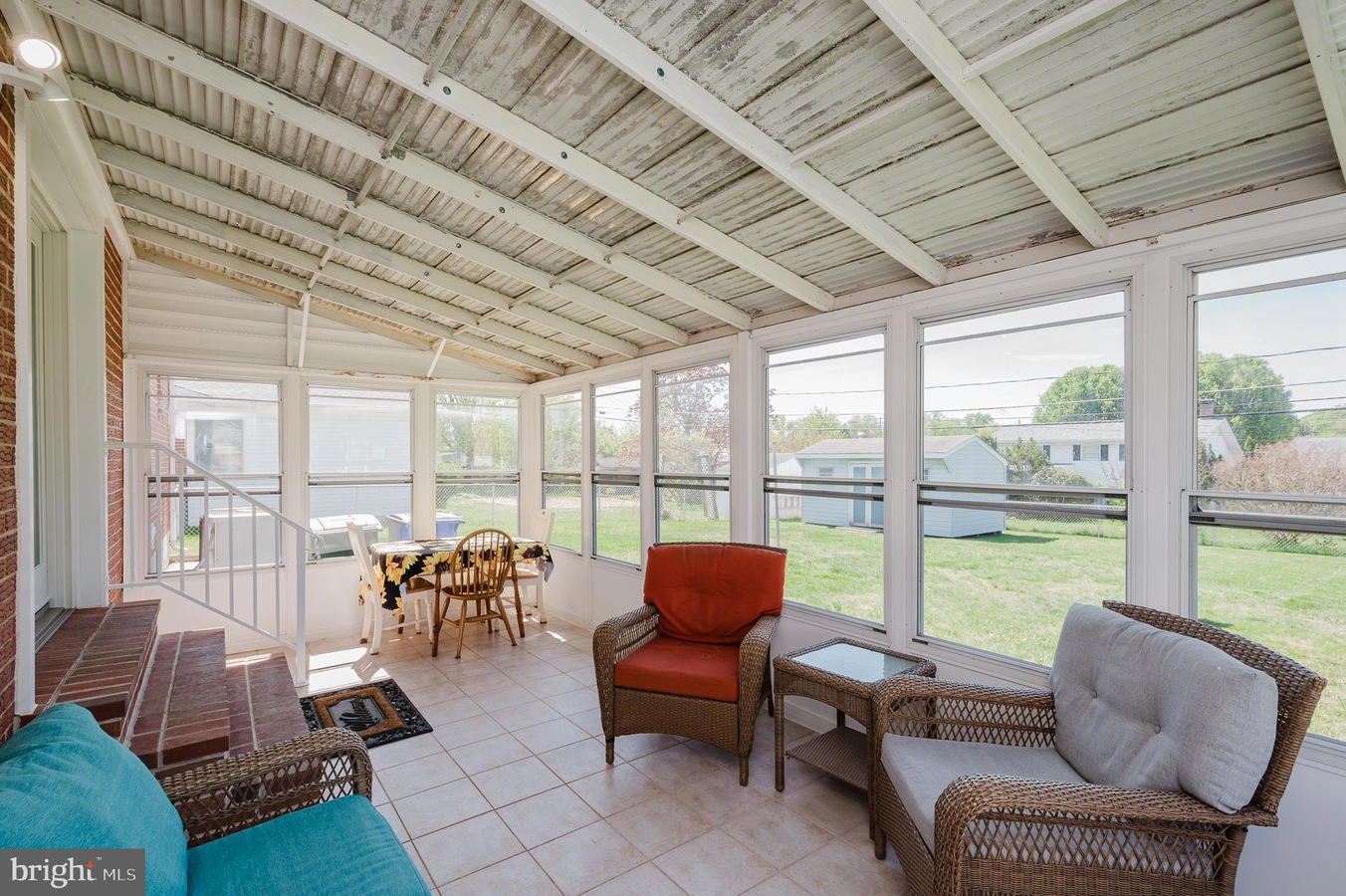Bright sunroom with white-framed windows, wicker seating, and a small dining table overlooking a grassy backyard