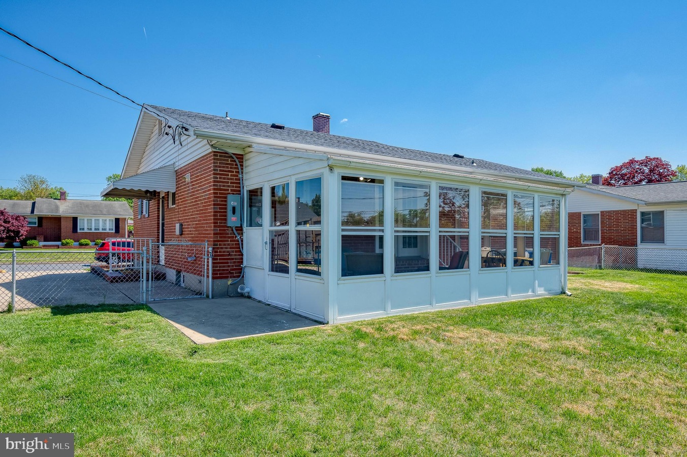 Brick, single-story building with a white-framed glass-enclosed sunroom along the side, set in a grassy yard under a clear blue sky.