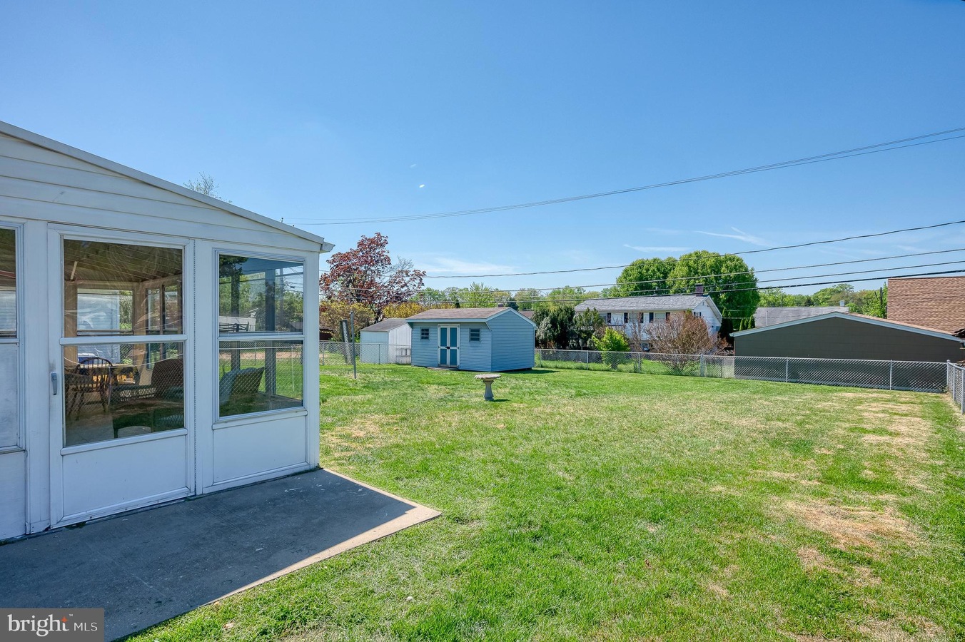 Backyard with a white enclosed porch on the left, open green lawn, and a small blue shed under a clear blue sky.