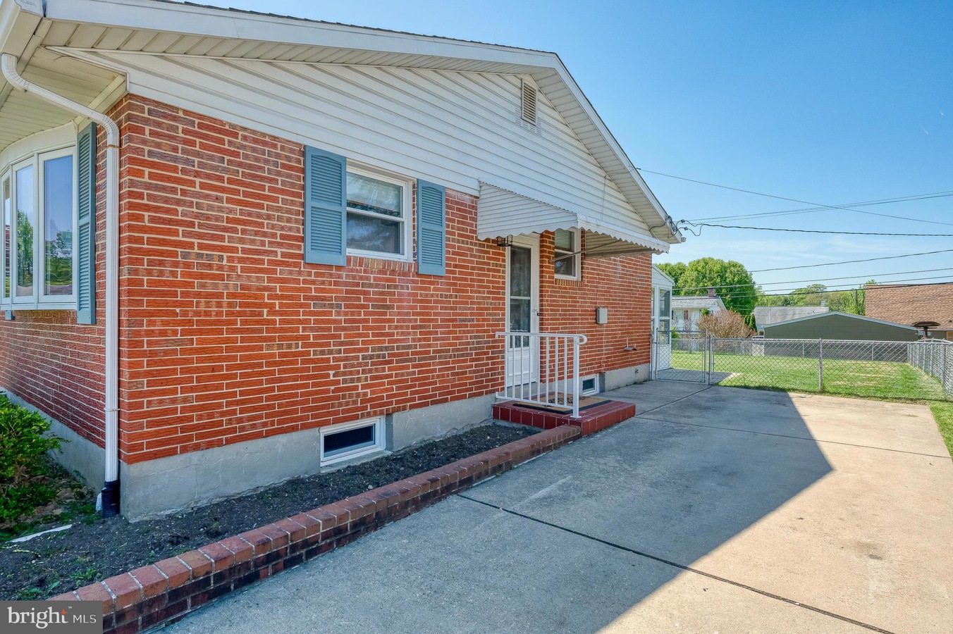 Brick ranch-style house with blue shutters, white awning over the entry, small front steps, and a concrete driveway.
