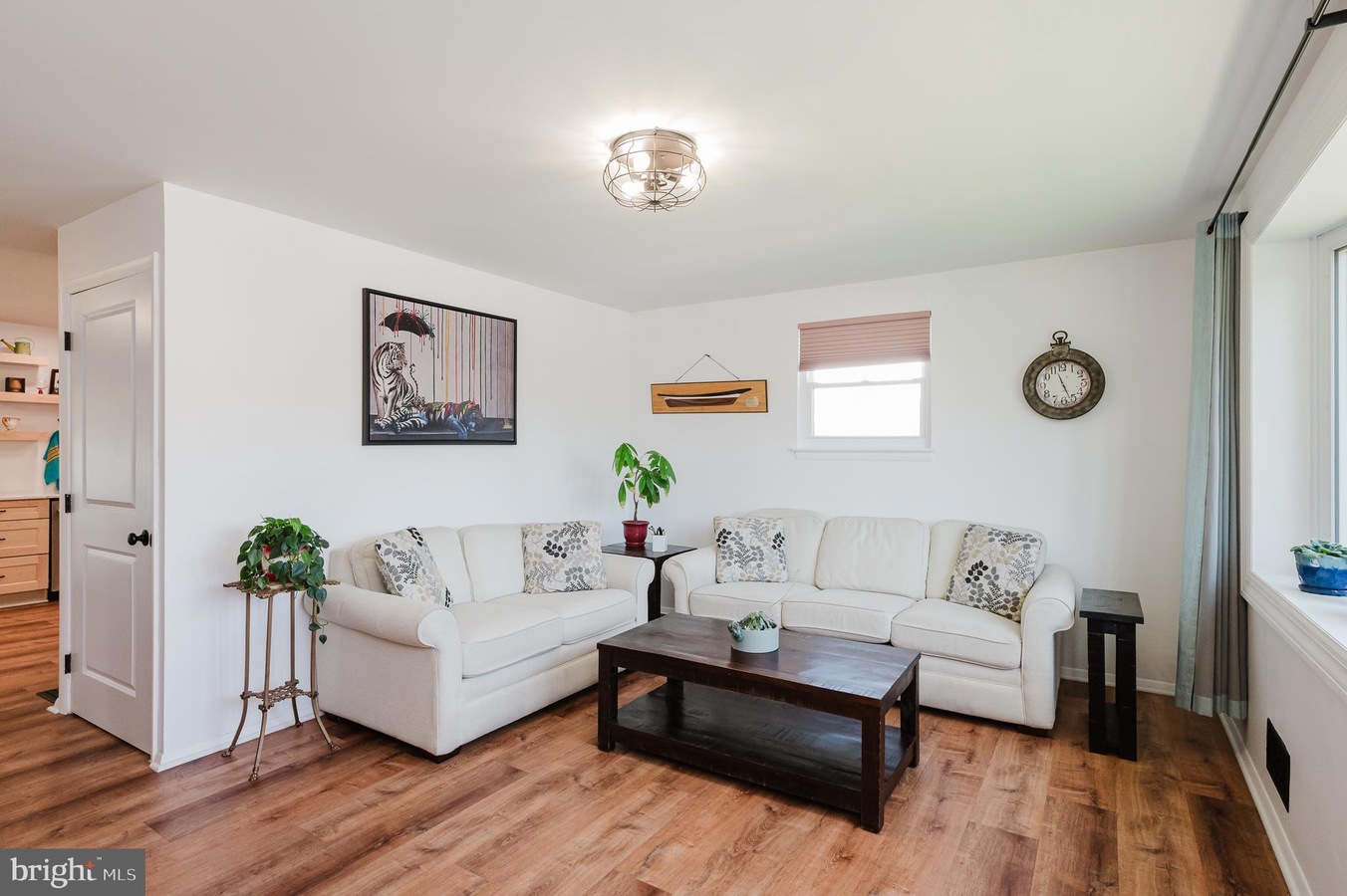 L-shaped white sofa set with patterned cushions, a dark wood coffee table, and potted plants in a bright living room.
