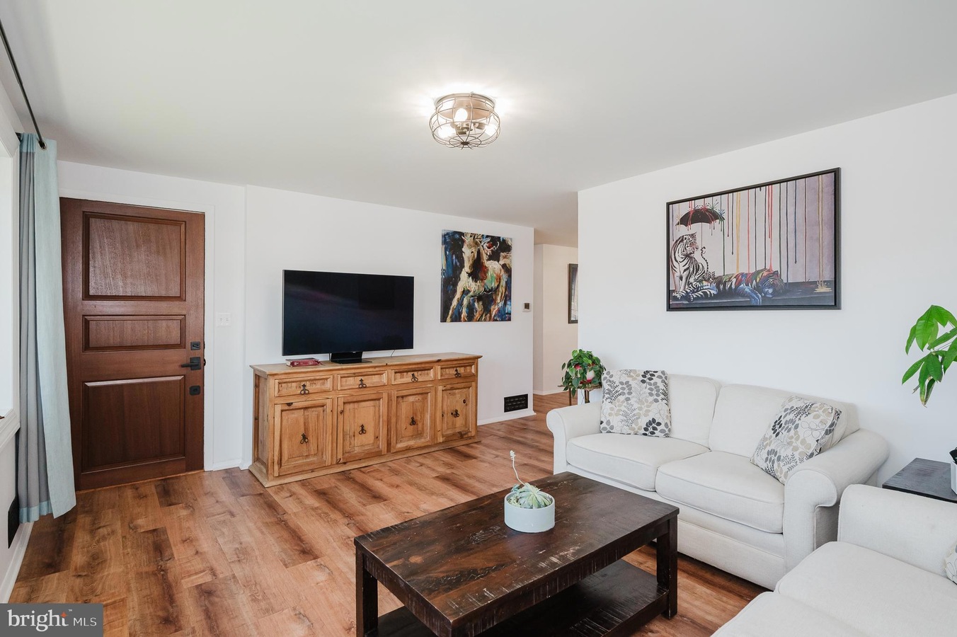 Living room with a flat-screen TV on a wooden cabinet, beige sofa, and a dark coffee table.