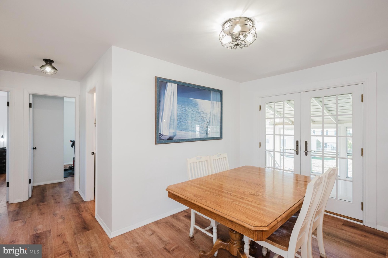 Bright dining room with a wooden table and white chairs, glass French doors, and a sea-themed wall art above the wall outlet edge.
