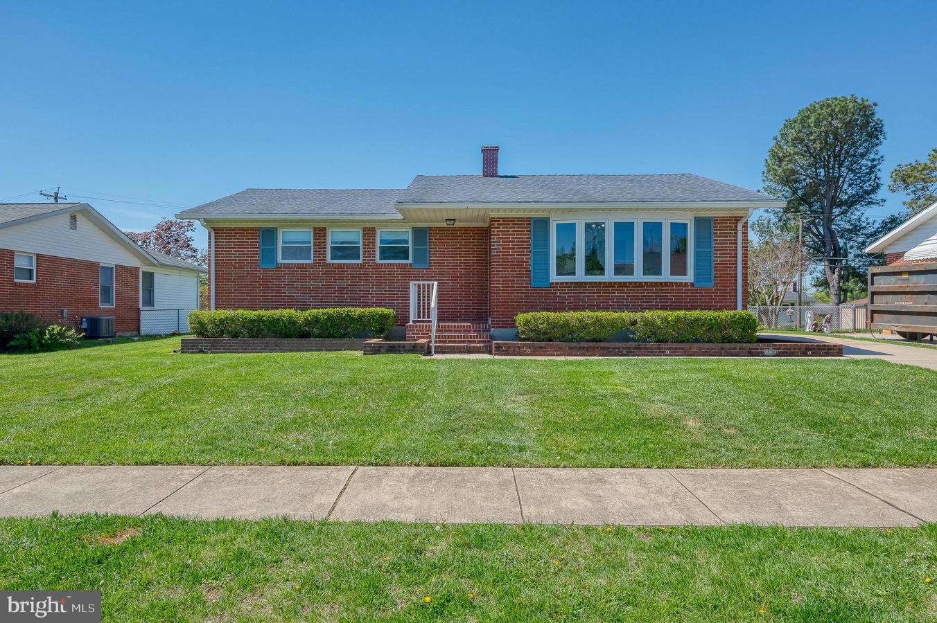 Front view of a single-story brick house with blue shutters, a small set of steps, and neatly trimmed hedges in front yard.