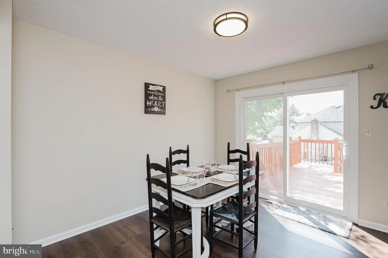Dining area with a square table set for four and black chairs, next to a sliding glass door opening to a wooden deck outside.