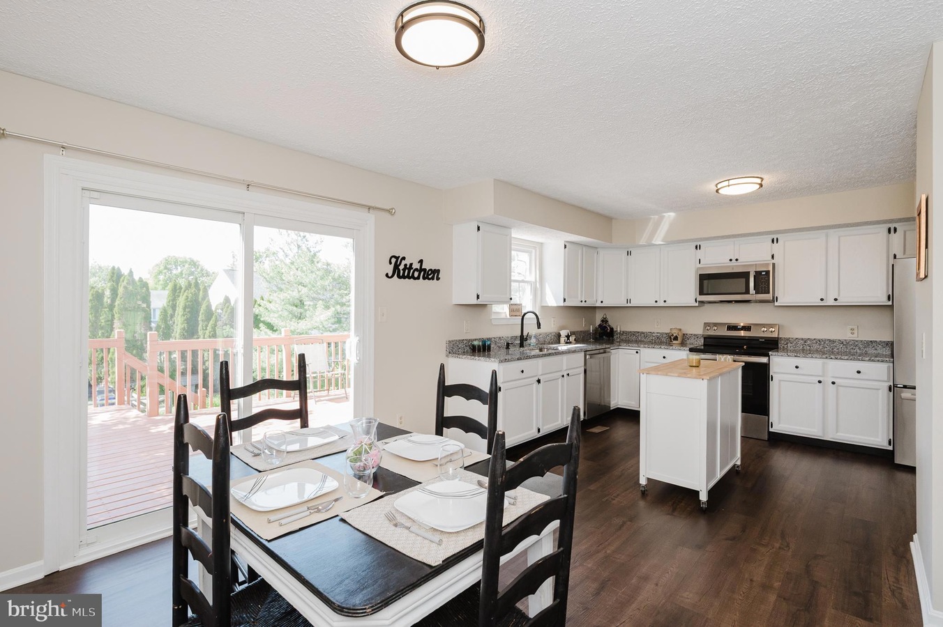 Bright kitchen and dining area with white cabinets, granite countertops, and a table set for four near a sliding glass door to the deck