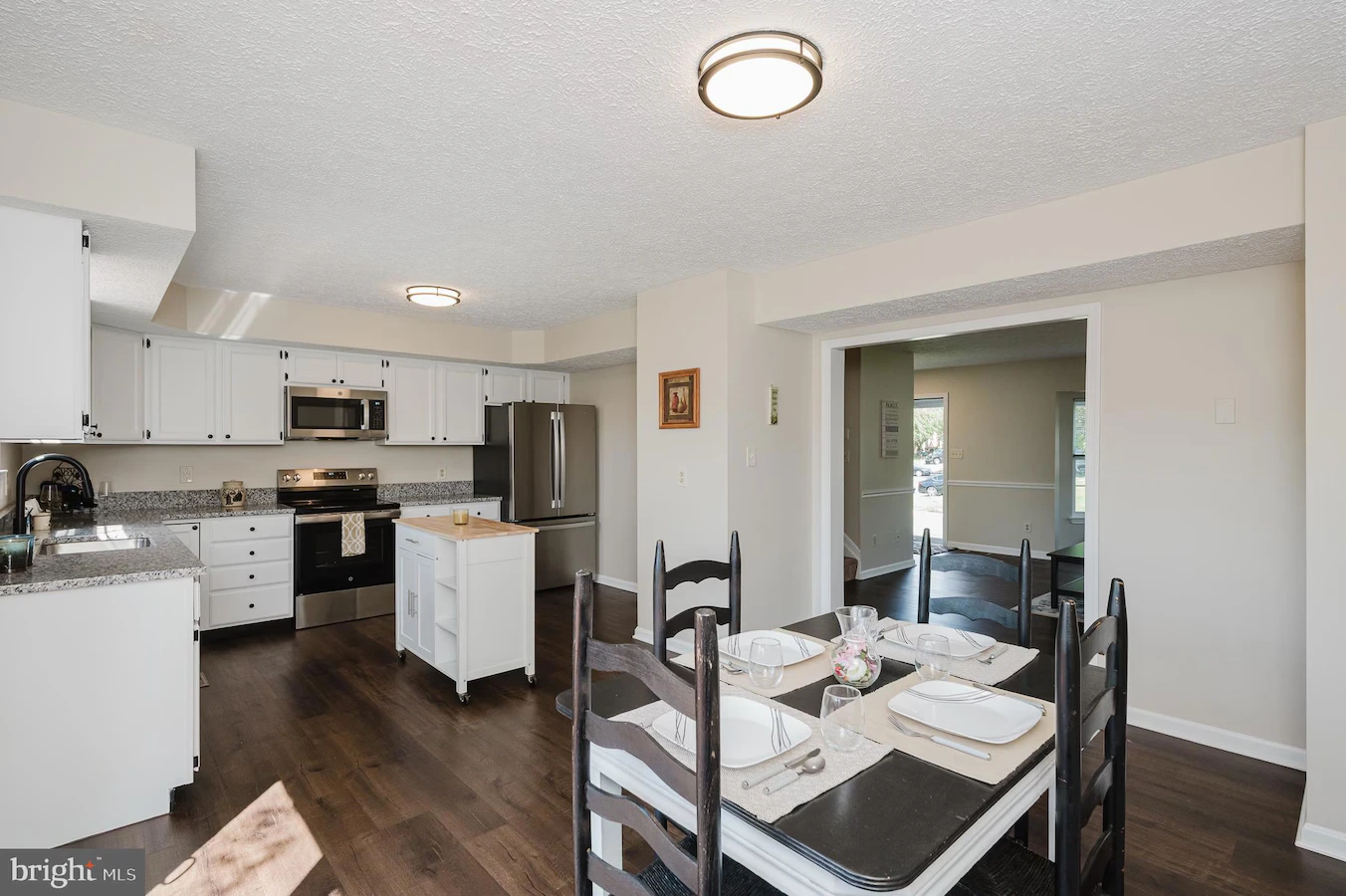 Open-concept kitchen and dining area with white cabinets, stainless steel fridge and range, and a table set for four in the foreground
