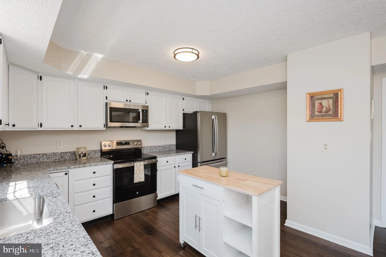 Bright kitchen with white cabinets, granite countertops, stainless steel fridge and range, and a small island with a wood top.