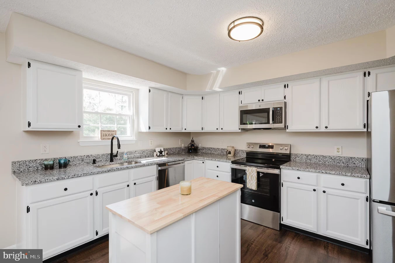 White kitchen with grey speckled countertops, island, and stainless steel appliances including fridge, oven, and microwave.