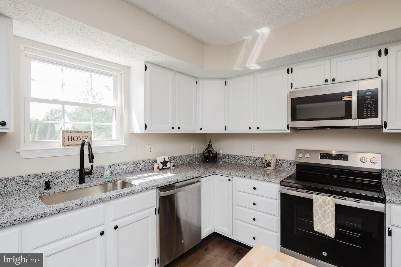 Bright, modern kitchen with white cabinets, granite counters, and stainless steel appliances including a dishwasher and range under a microwave.