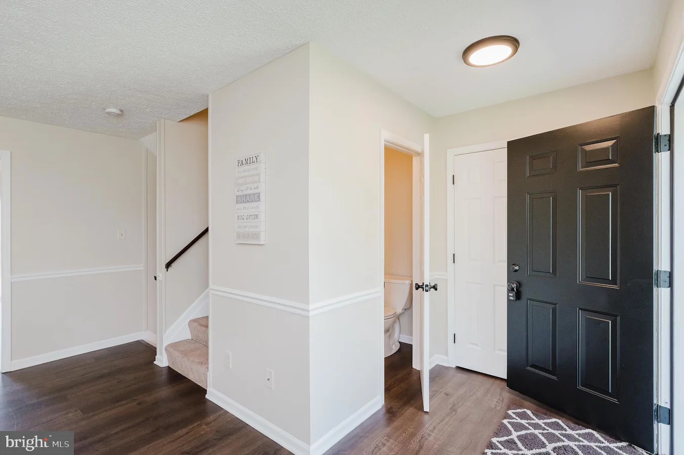 Entryway with a black front door open to a hallway; white walls, wood floor, and stairs to the left.