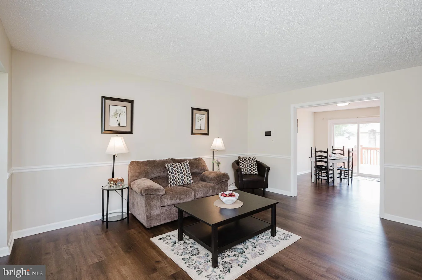 Cozy living room with a brown sofa, matching chair, two lamps, and a black coffee table on a floral rug.