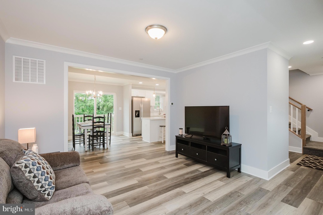 Open-concept living room with gray walls, wood-look flooring, and a black TV stand with a large flat-screen TV.