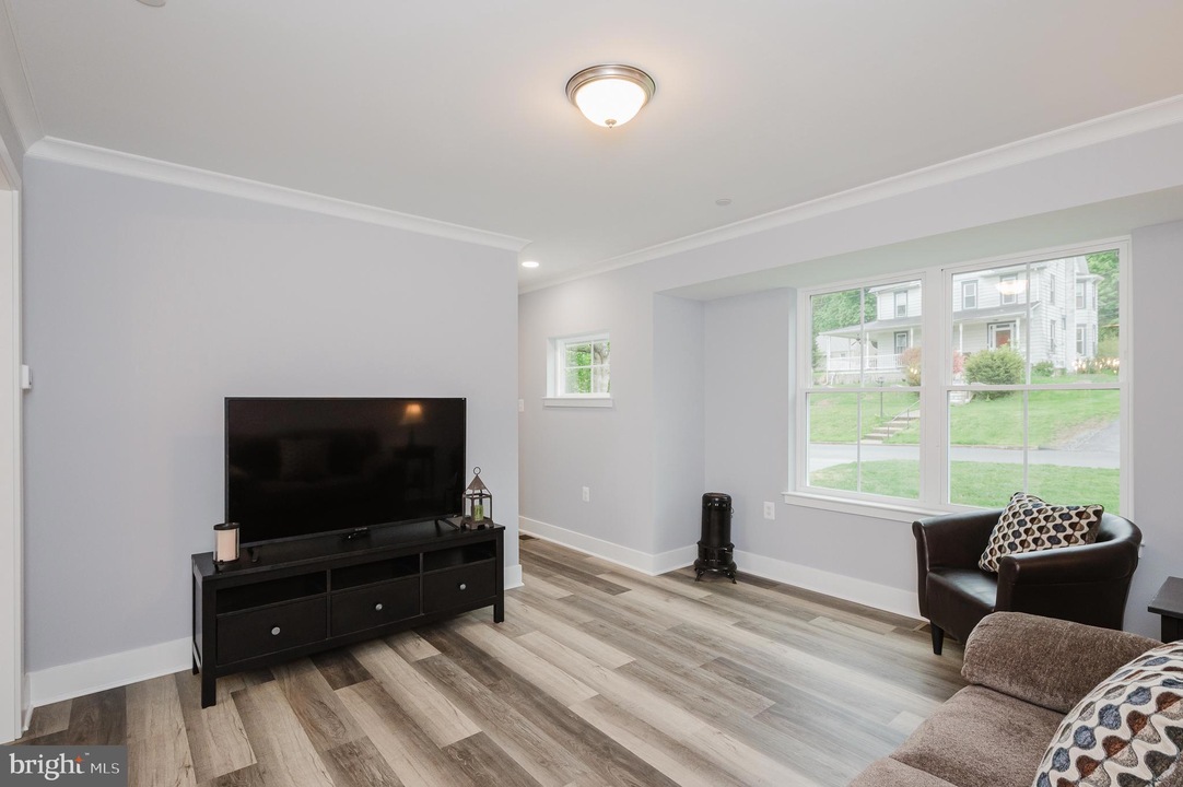 Living room with a flat-screen TV on a black media console, beige sofa, and a large window letting in daylight outside edge light fixture above.