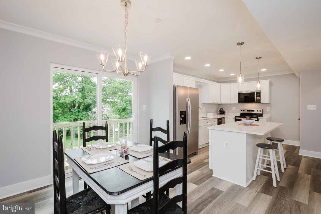 Bright open dining and kitchen area with a white table set for four, black chairs, and a chandelier near a sliding glass door to a green backyard.