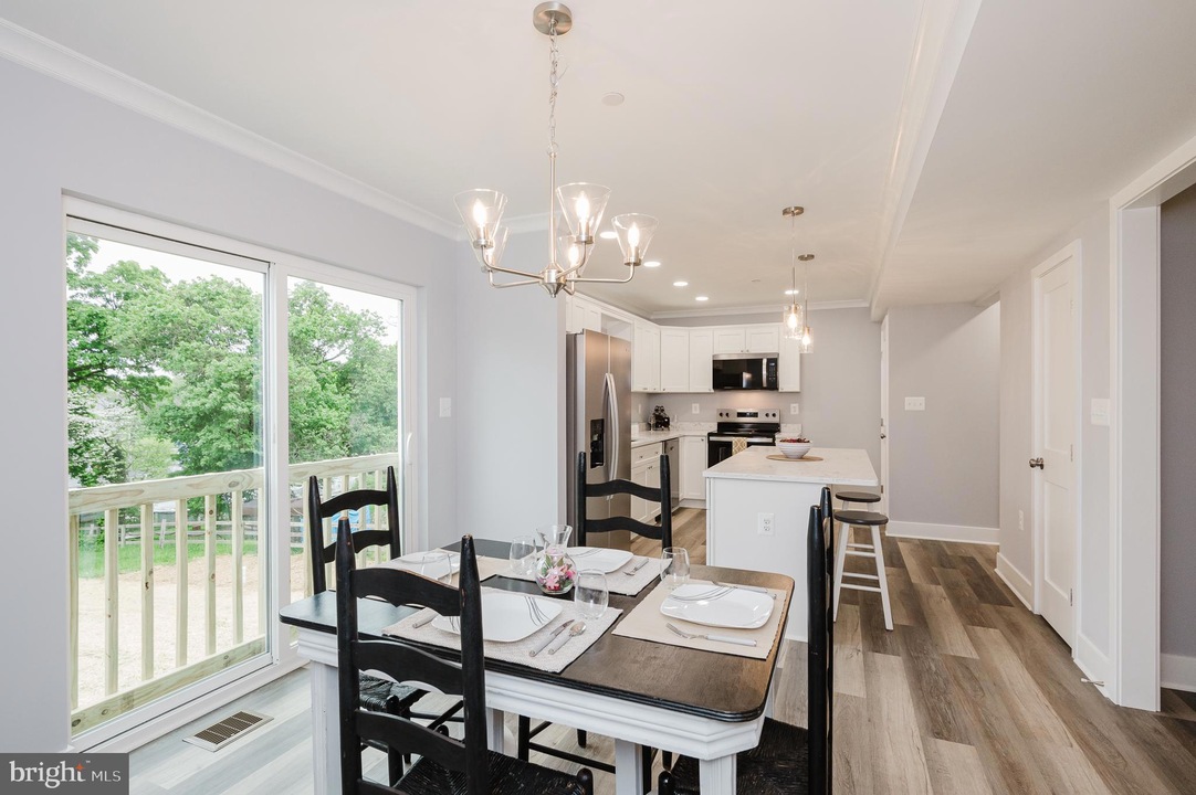 Open-concept kitchen and dining area with a sliding glass door to a deck, white cabinets, stainless steel appliances, and a chandelier over the table.