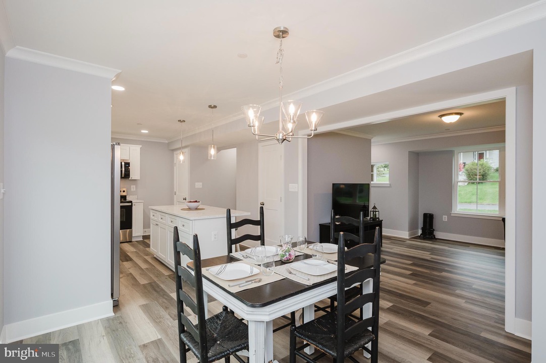 Open-concept dining area with a rectangular table set for four, black chairs, and a bright kitchen island in a light-gray home interior.