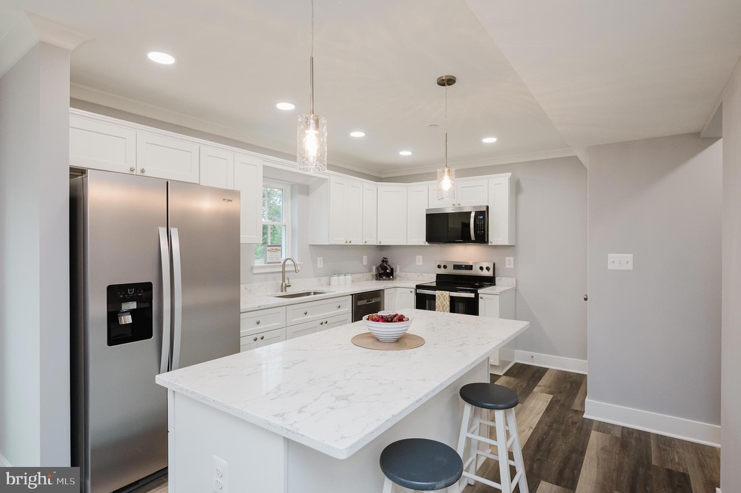 Modern white kitchen with marble island, stainless steel fridge, stove, and pendant lights above the island.