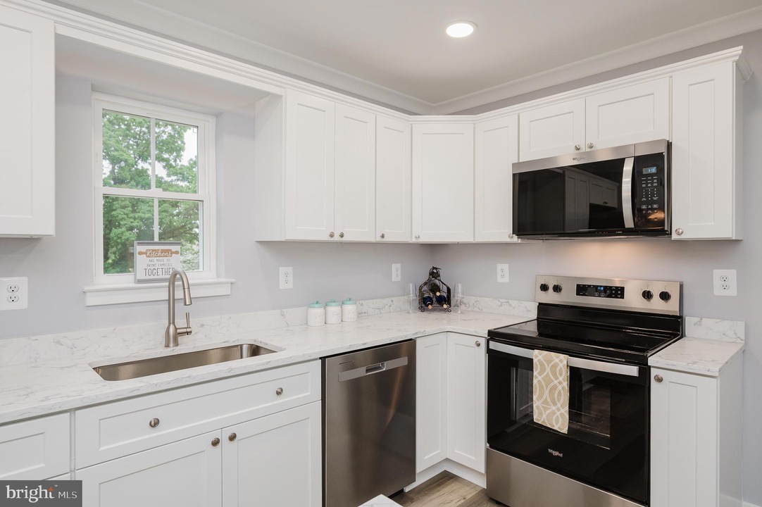 White kitchen with marble countertops, stainless steel appliances, and a window above the sink.