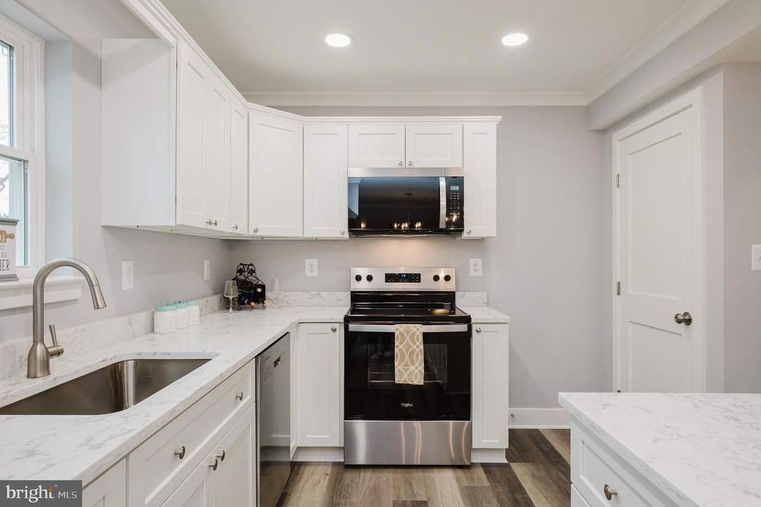 Modern white kitchen with marble countertops, stainless steel range and microwave, and a double sink on the left.