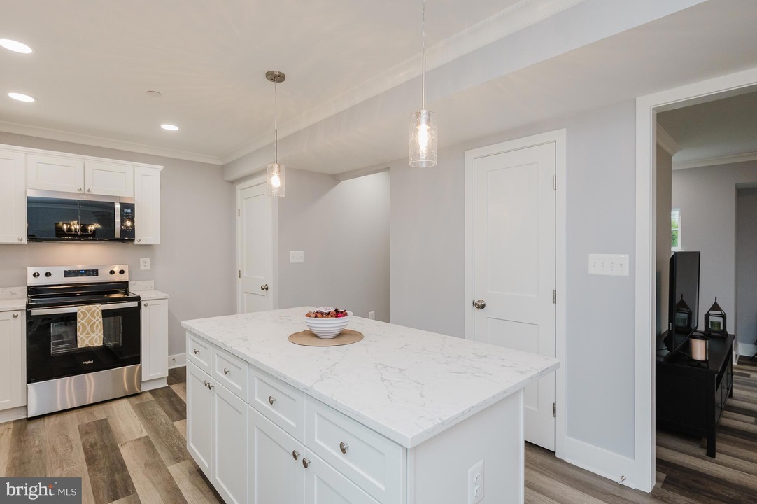Bright kitchen with a marble-topped island, white cabinets, and pendant lights over the island.