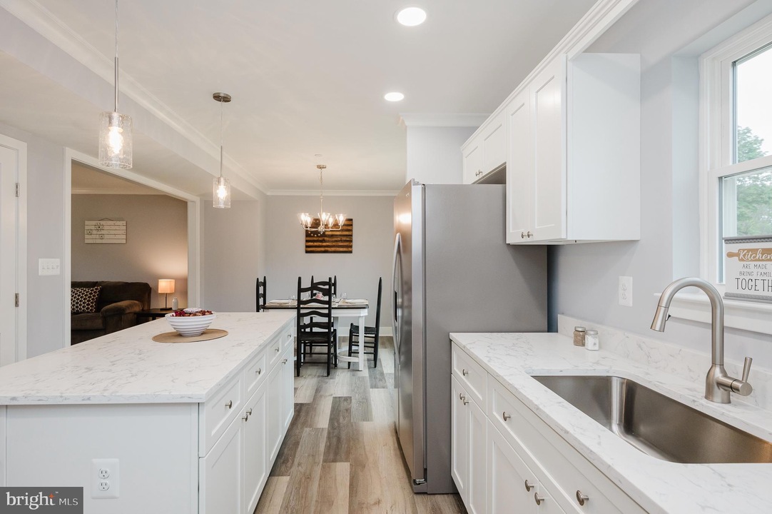 Bright modern kitchen with white cabinets, marble countertops, an island, and a stainless steel refrigerator; dining table visible in the back.