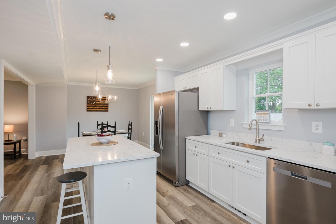 Bright white kitchen with marble island, stainless steel appliances, and a dining nook in the background.