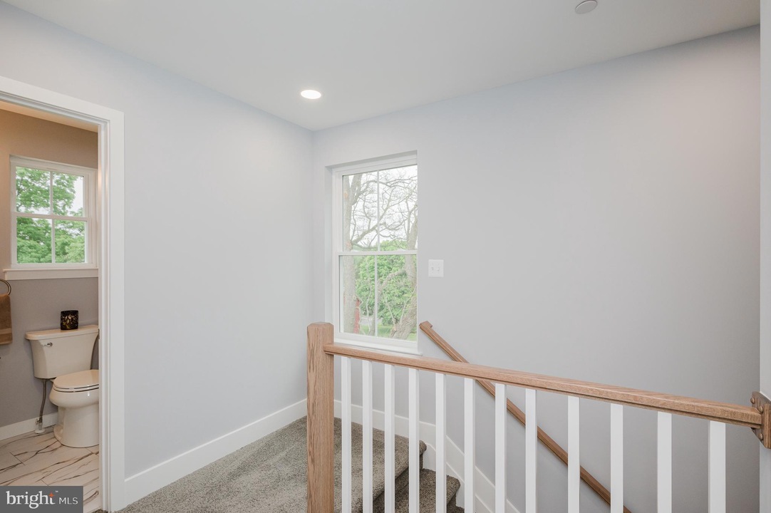 Upstairs landing with a wooden railing, window letting light in, and a small bathroom to the left.