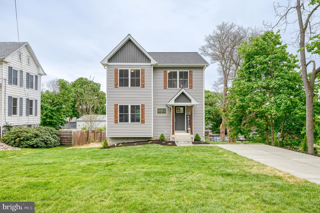 Two-story gray house with brown shutters and a small front porch, a concrete path and manicured lawn leading to the entrance.
