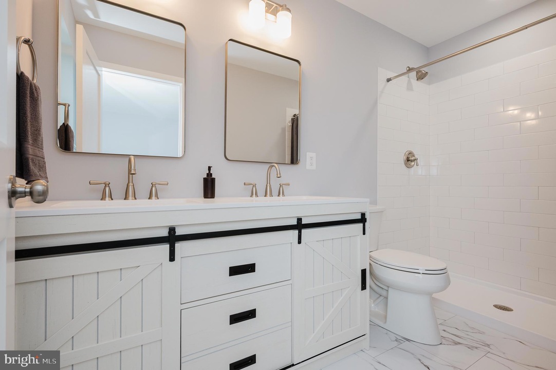 Double-sink bathroom vanity with white cabinets, black hardware, and sliding barn-door drawers, in a light gray room with two rectangular mirrors and brushed-nickel faucets.
