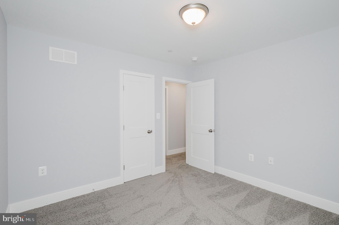 Empty bedroom with pale gray walls, white doors, and light gray carpet; ceiling light centered above.