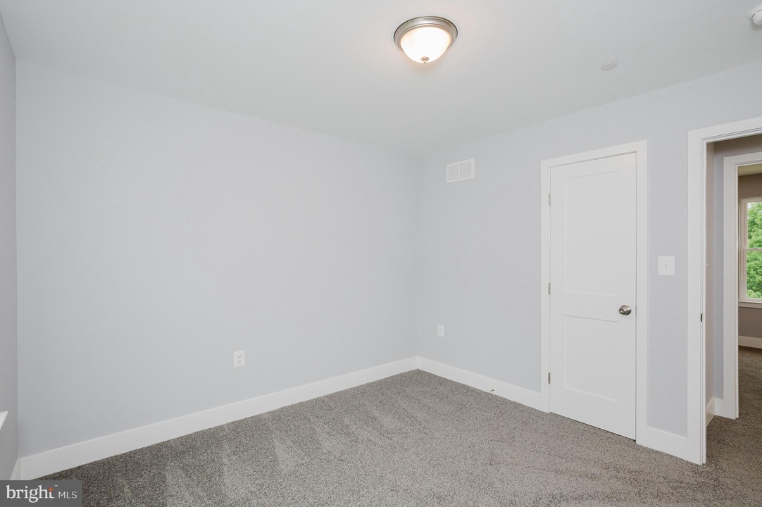 Small empty bedroom with light gray walls, white trim, beige carpet, and a ceiling light fixture in the center of the ceiling.