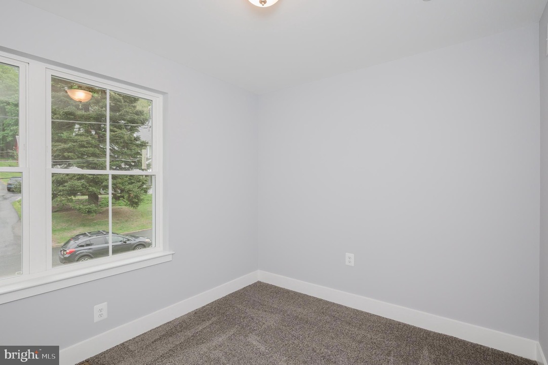 Empty light-gray room with white baseboards and a large window showing a parked car and greenery outside