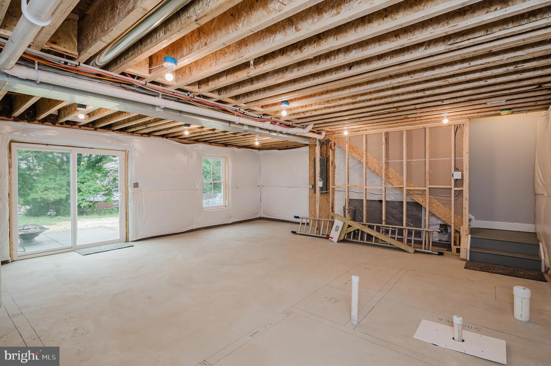 Unfinished basement with exposed joists, plastic-wrapped walls, and a sliding glass door to the outside area.