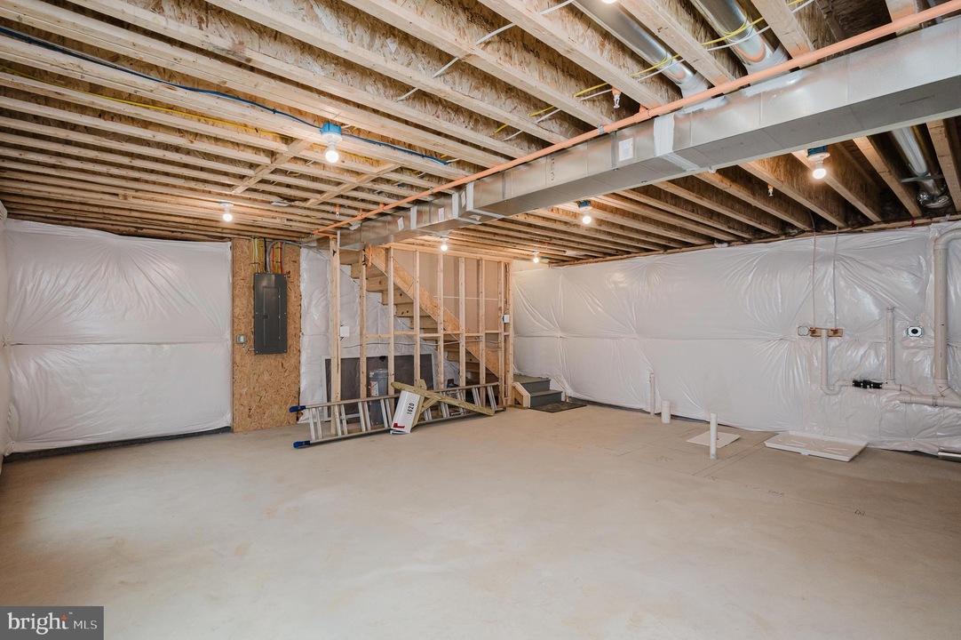 Unfinished basement with exposed ceiling joists, plastic walls, and construction tools scattered, including a ladder and stairs to an upper level for renovation work.