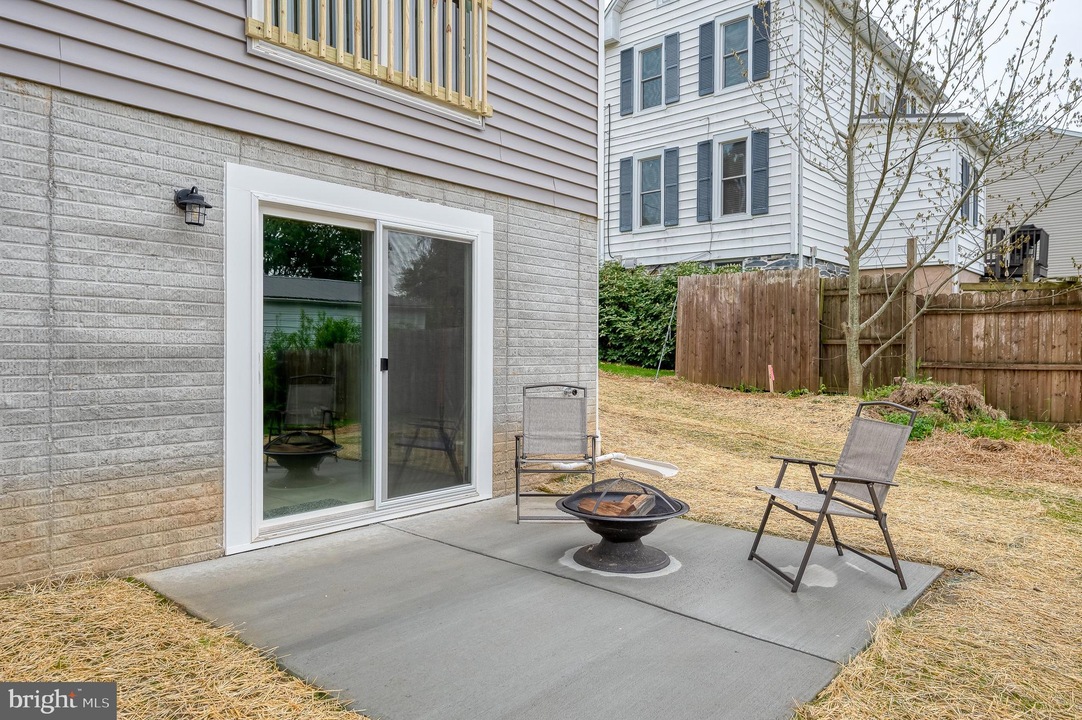 Backyard patio with sliding glass door, two metal chairs, and a round fire pit on a concrete slab.