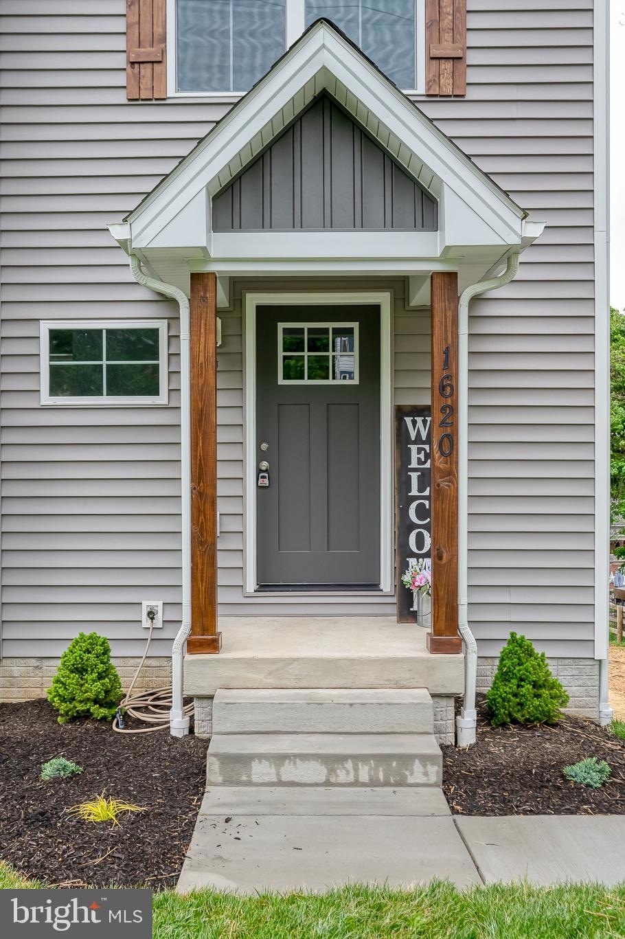 Front entry with gray door, two wooden posts, and a vertical 'WELCOME' sign beside the steps. House number 1620 visible.