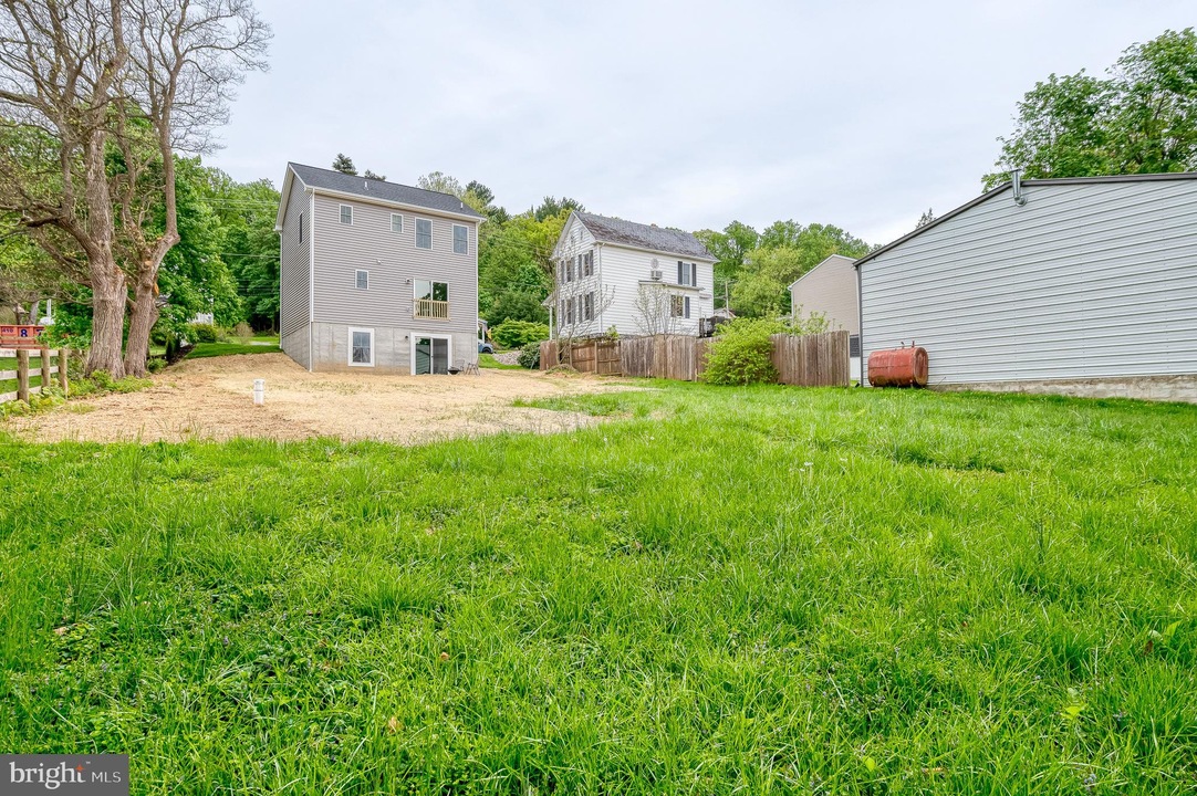 Wide view of a green backyard with two-story gray houses, a wooden fence, and a white shed in a suburban neighborhood.