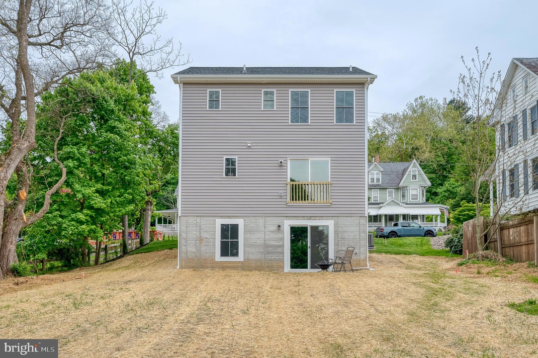Three-story gray-siding house with a concrete basement level, back yard, sliding glass door, and a small balcony above the ground floor patio.