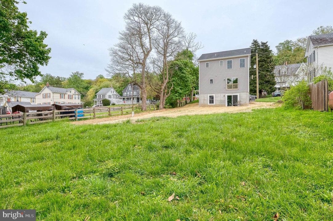 Green grassy lot in a residential area with a gray house under construction in the background and trees nearby as neighbors look on.