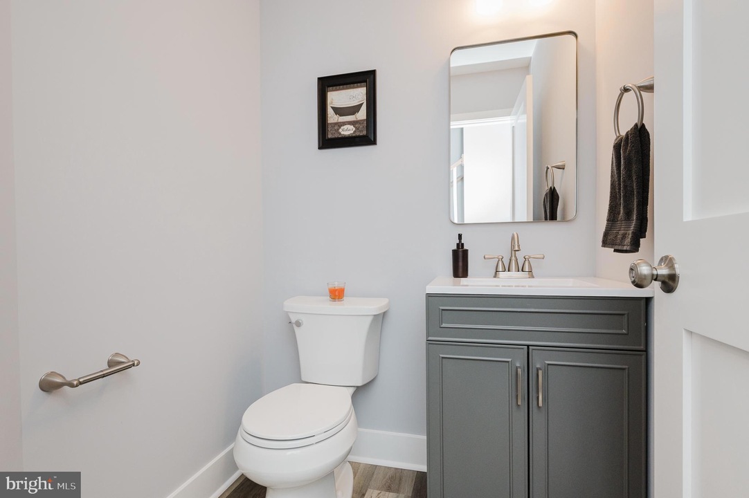Small bathroom with a gray cabinet vanity, white sink, mirror, and toilet against pale walls.